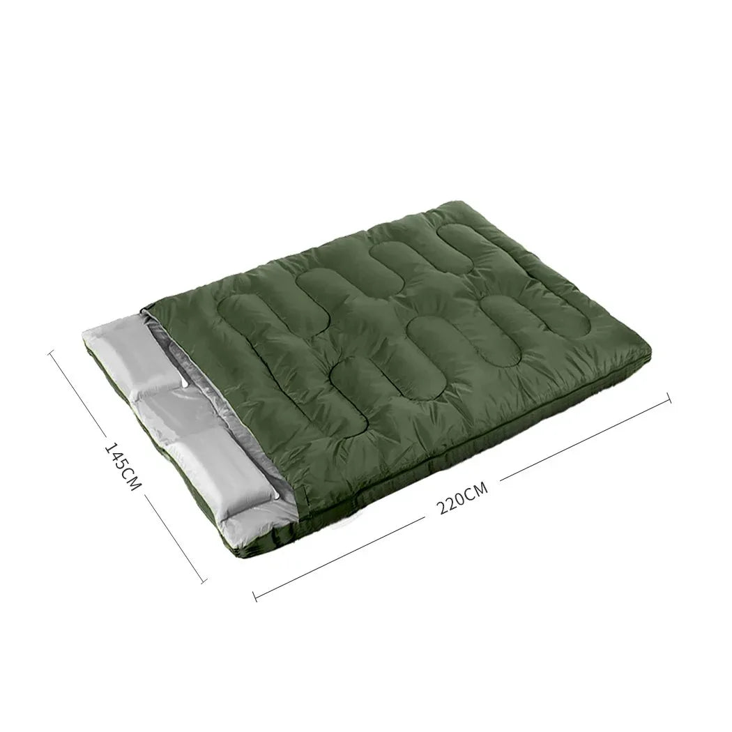 Two adults lying inside joined double sleeping bag outdoors surrounded by nature
