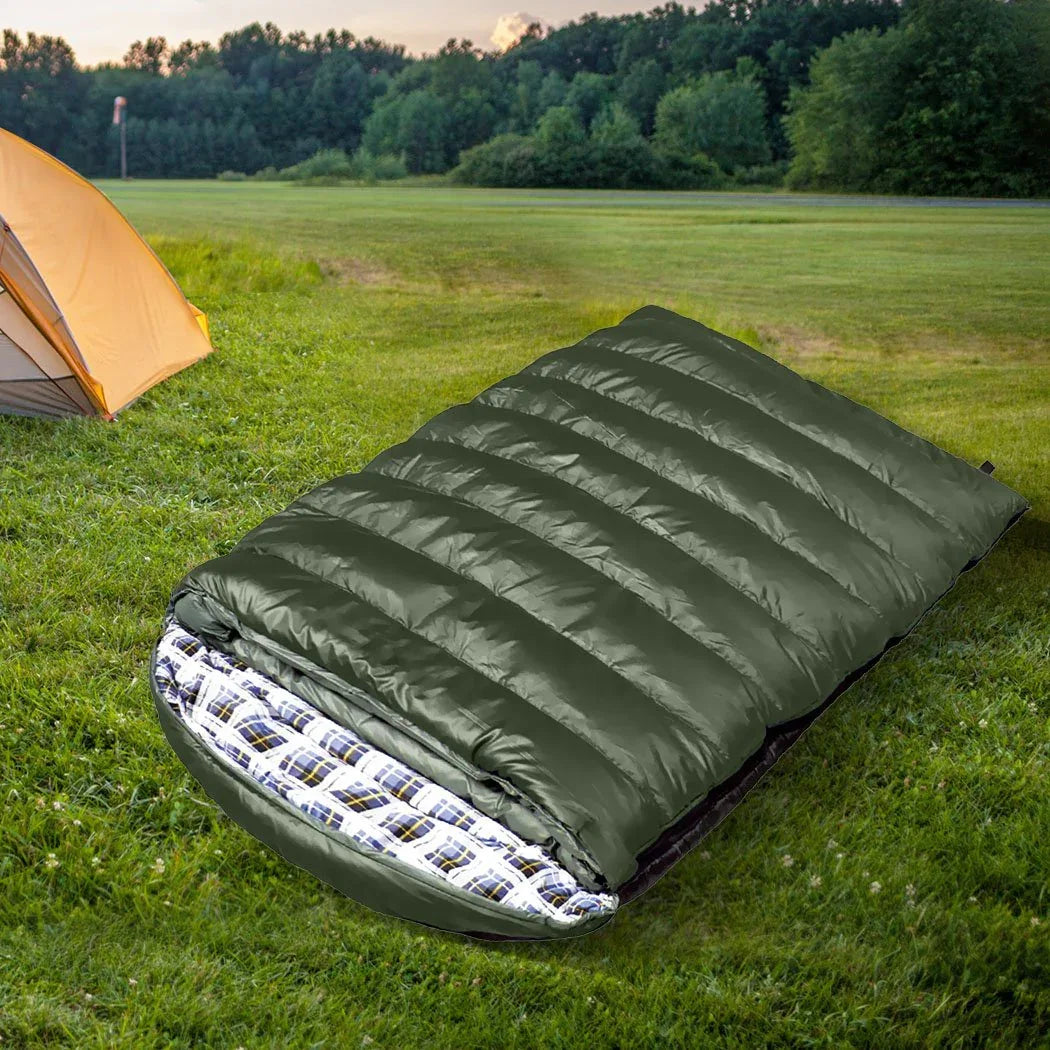 Outdoor camping setup with two sleeping bags laid out on grass near a tent.