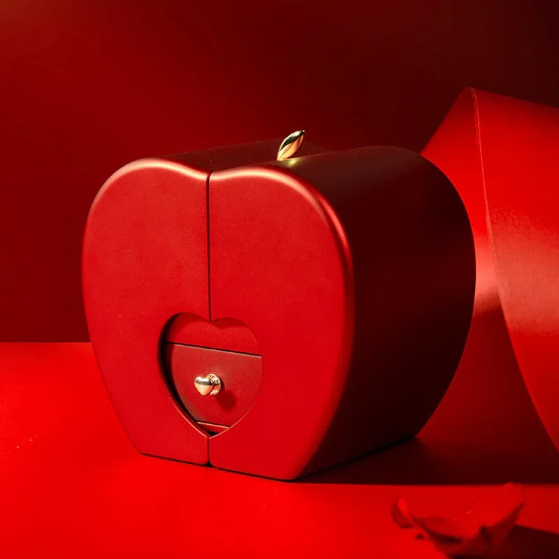Red apple jewelry box with artificial rose displayed on a white surface.