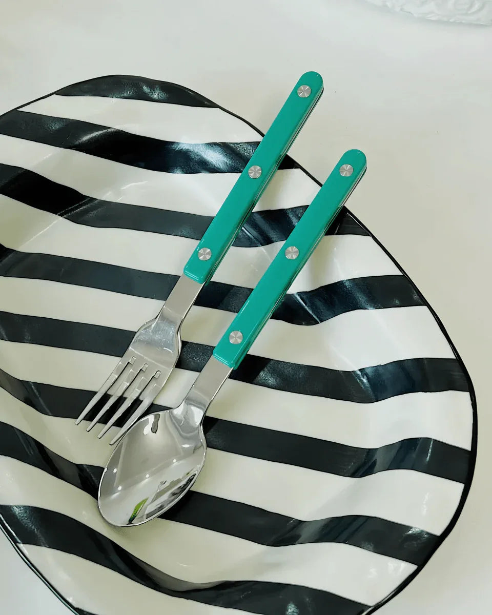 Overhead view of turquoise French rivet cutlery neatly lined up on a white surface.