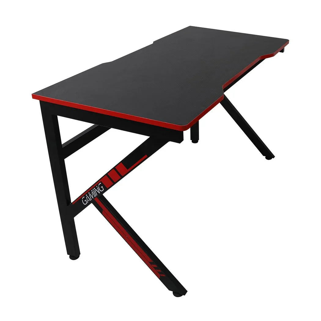 Black gaming desk with spacious tabletop and carbon fiber textured surface in bright room.