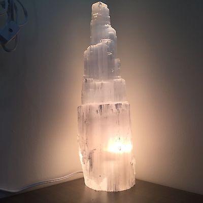 Selenite skyscraper lamp turned on, radiating a warm, calming glow on a clean white background.