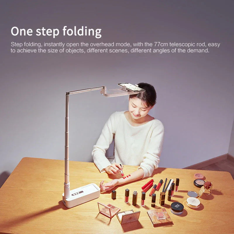 Selfie phone holder extended with ring light on, standing on a wooden table.