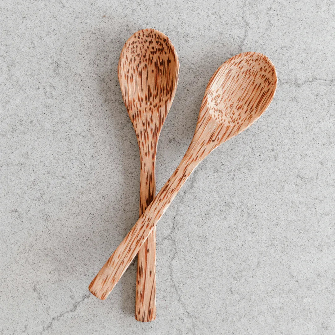 Hand using a wooden coconut spoon to scoop food from a bowl, emphasizing sustainable cutlery.