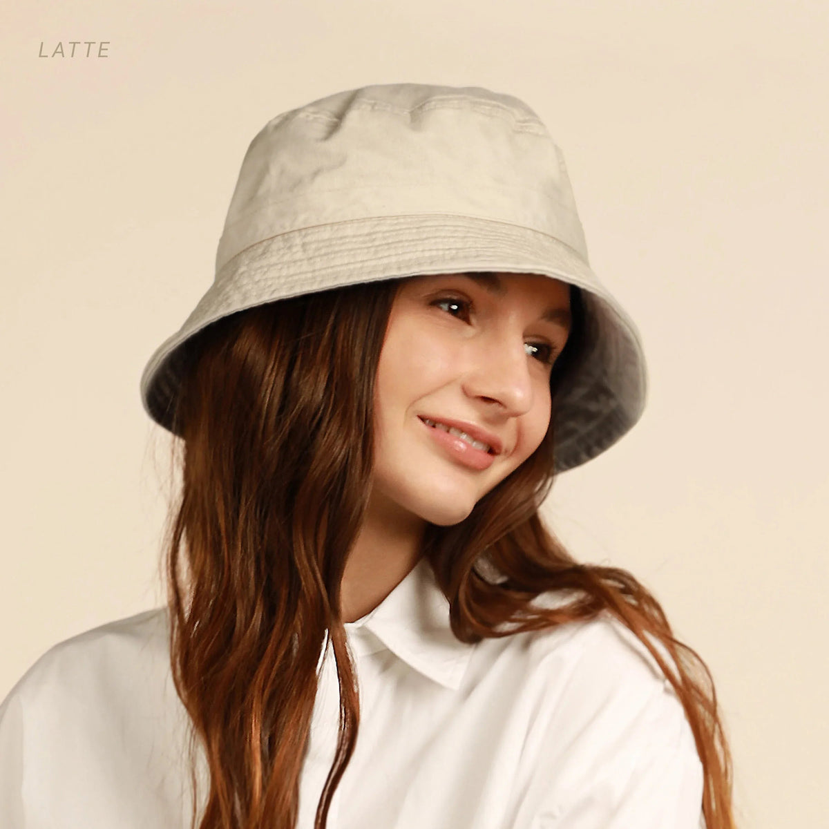 Model wearing light beige cotton bucket hat with flat brim outdoors.