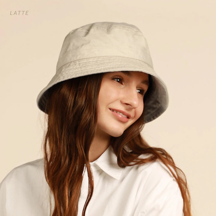 Model wearing light beige cotton bucket hat with flat brim outdoors.