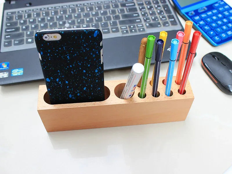 Wooden pen container attached to phone holder, filled with pens and a smartphone standing upright.