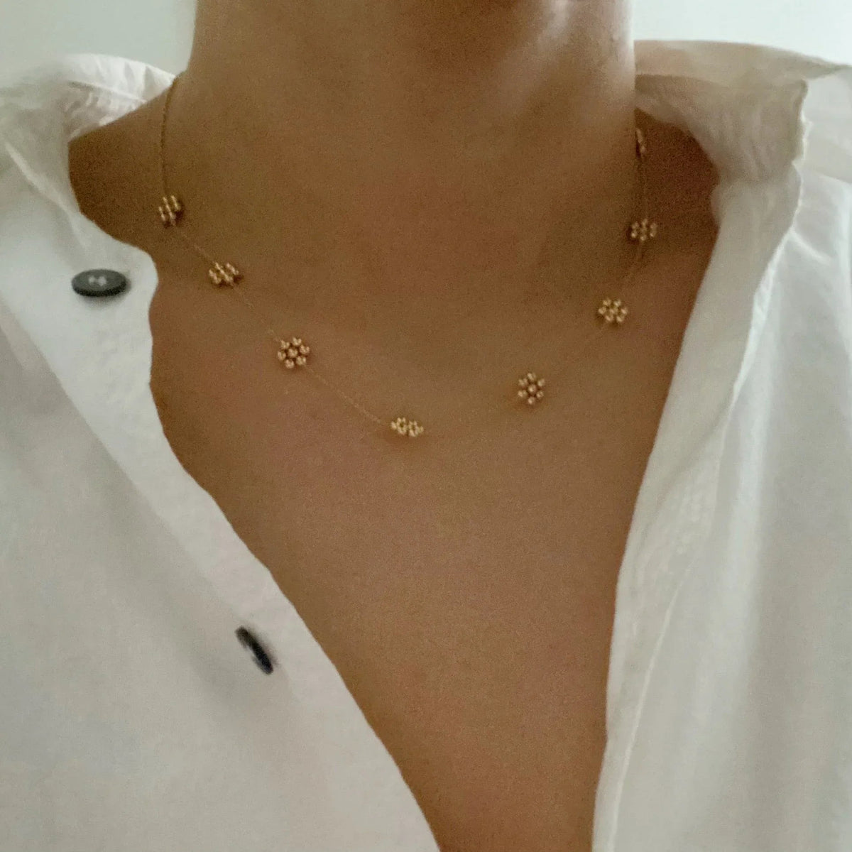 Model wearing dainty golden bead flower necklace layered with other chains on neck.