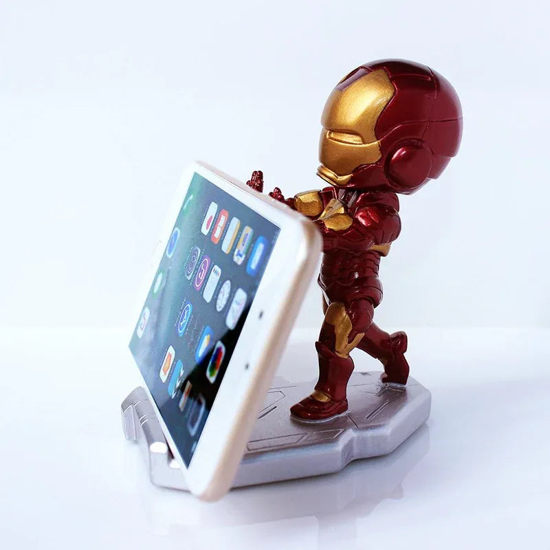 Front view of Iron Man figure phone stand in red and gold resin holding a smartphone, placed on a wooden desk.