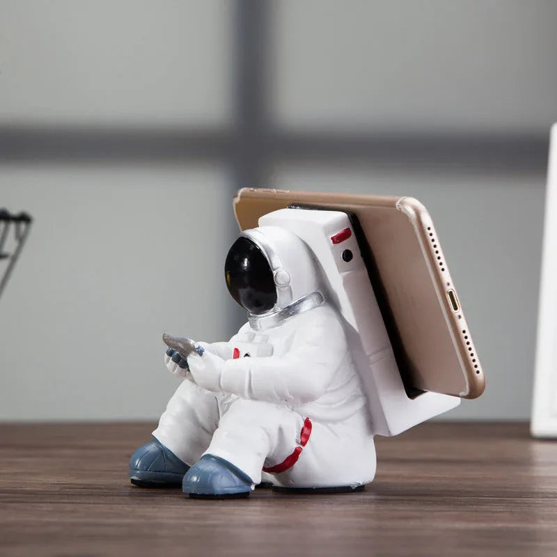 Astronaut desktop phone holder positioned on a light wooden table with natural light.