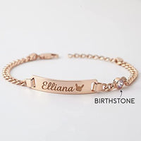 Sterling silver baby bracelet with engraved name and birthstone charm on a dark fabric background.