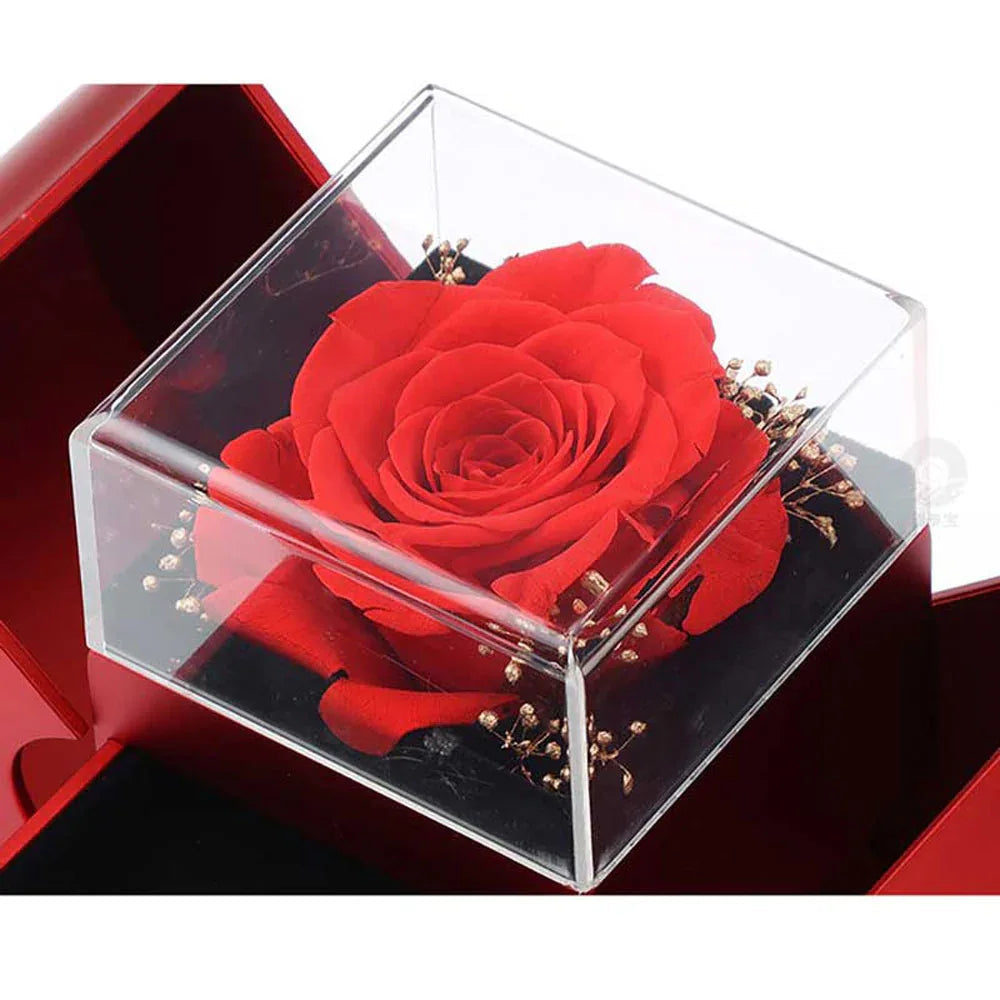 Artificial rose in red apple-shaped gift box with Christmas decoration in background.