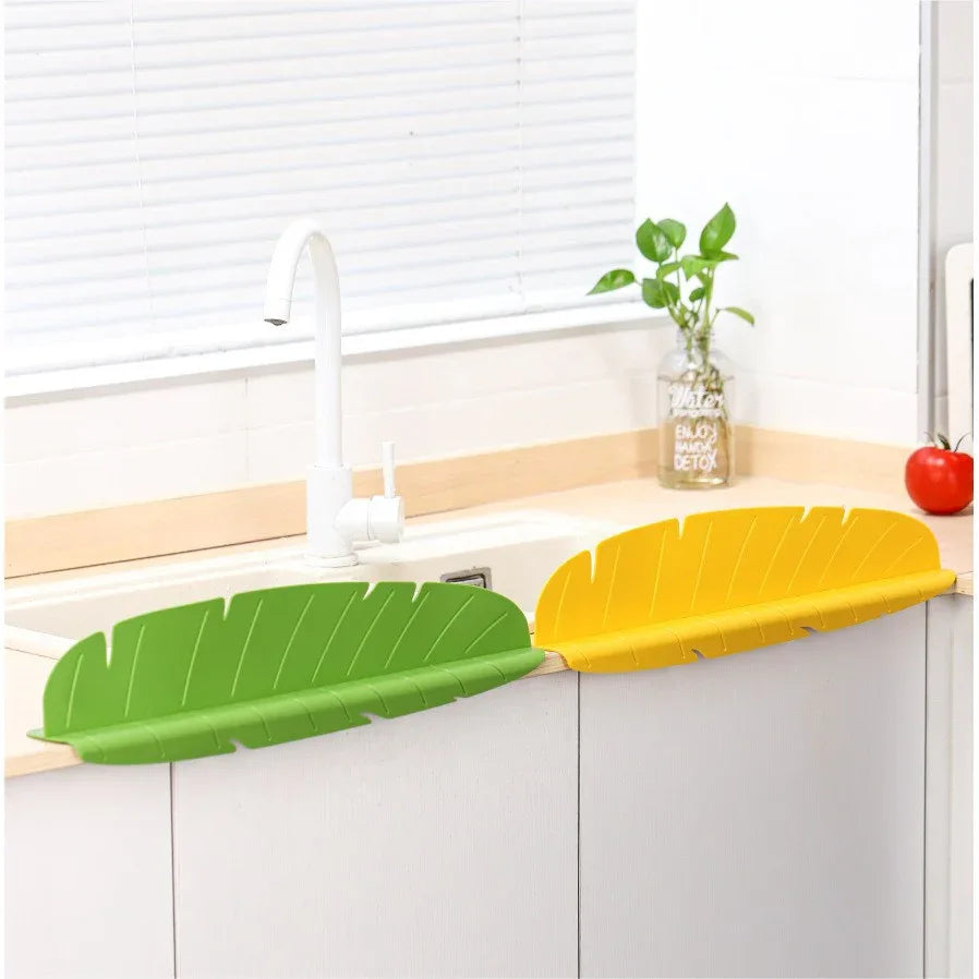 White silicone kitchen sink splash guard shaped like a banana leaf placed on sink edge.