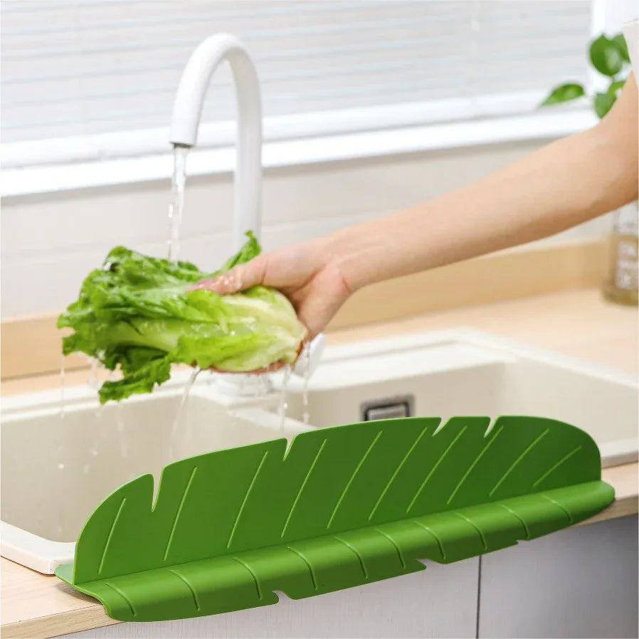 Green silicone kitchen sink splash guard with suction cups on a white sink edge.