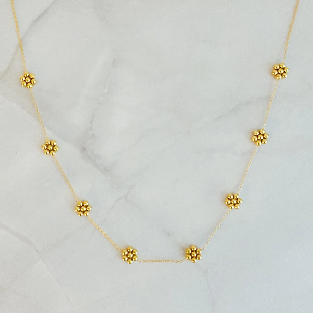 Close-up of delicate golden necklace with tiny bead flowers on a soft white background.