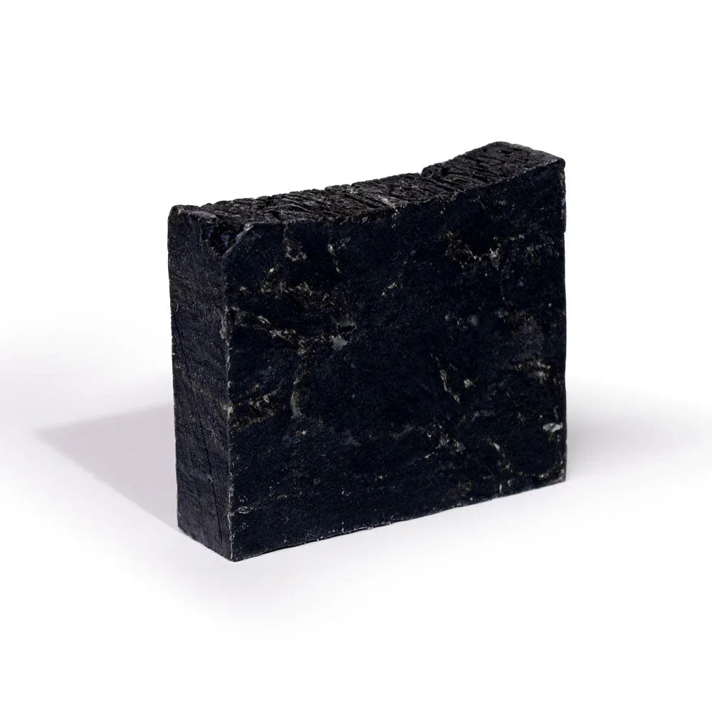 Black charcoal powder displayed on white surface, highlighting the soap’s activated charcoal ingredient.