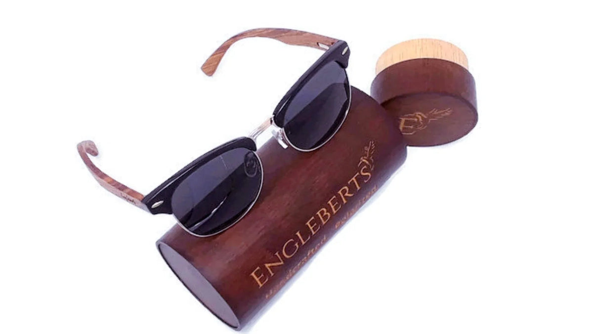 Walnut wood sunglasses with polarized lenses resting beside bamboo case and accessories on wooden surface.