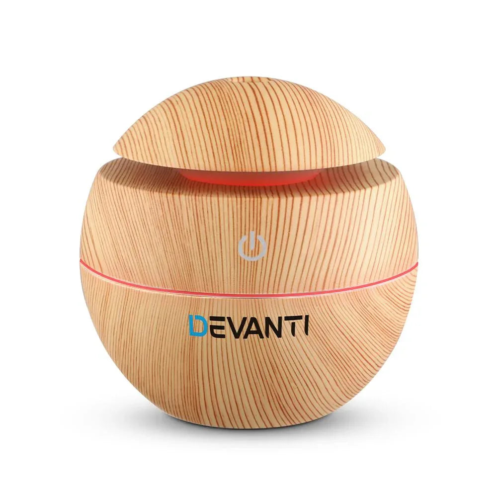 Devanti aromatherapy diffuser with wood grain finish emitting mist on a wooden table.