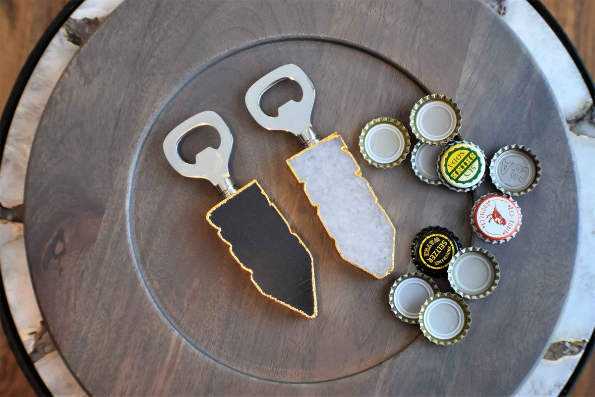 Bottle opener with white quartz handle and gold trim angled on a wooden surface.