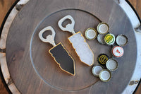 Bottle opener with white quartz handle and gold trim angled on a wooden surface.