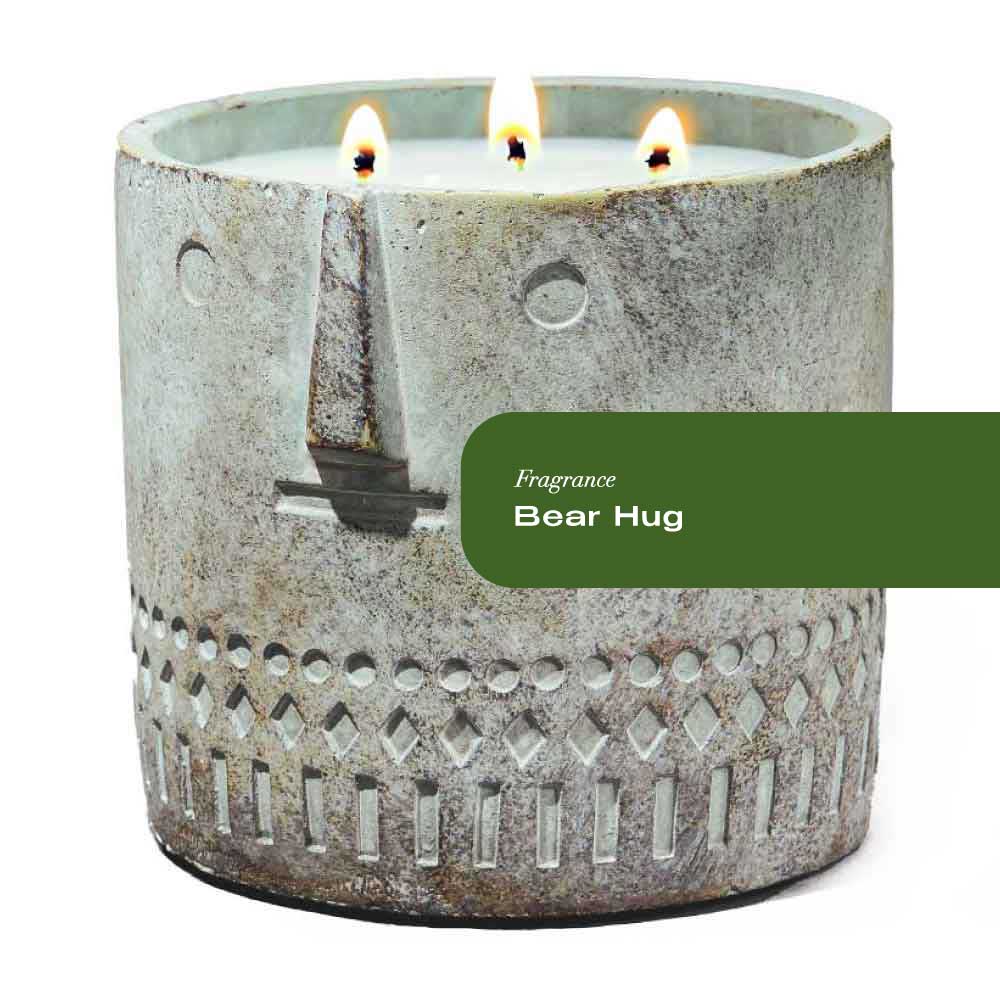 Close-up of a textured stone face candle shaped like a bear with an evergreen background.