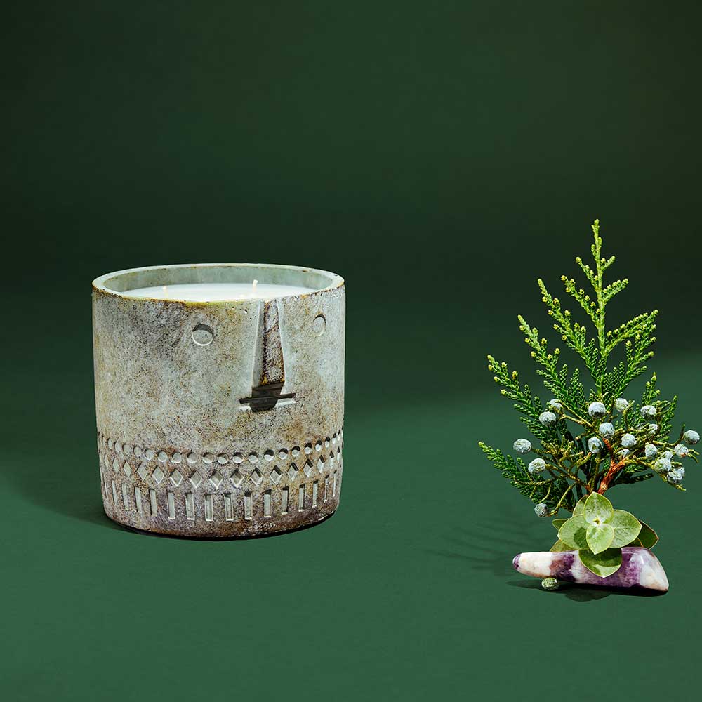 Close-up of cement vessel candle showing textured, artistic face detail on neutral background