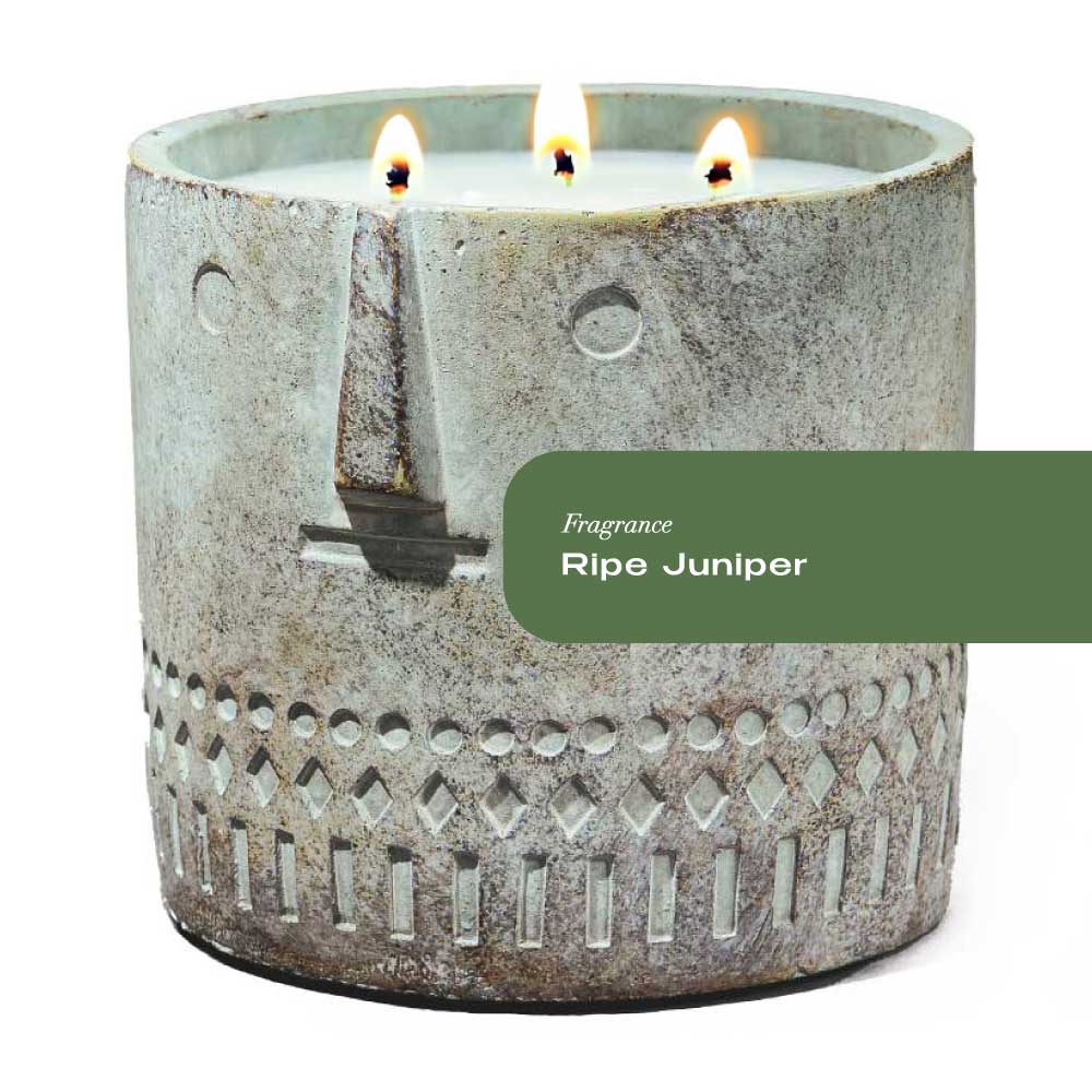 Hand-painted cement vessel candle with a rustic face design on a wooden surface