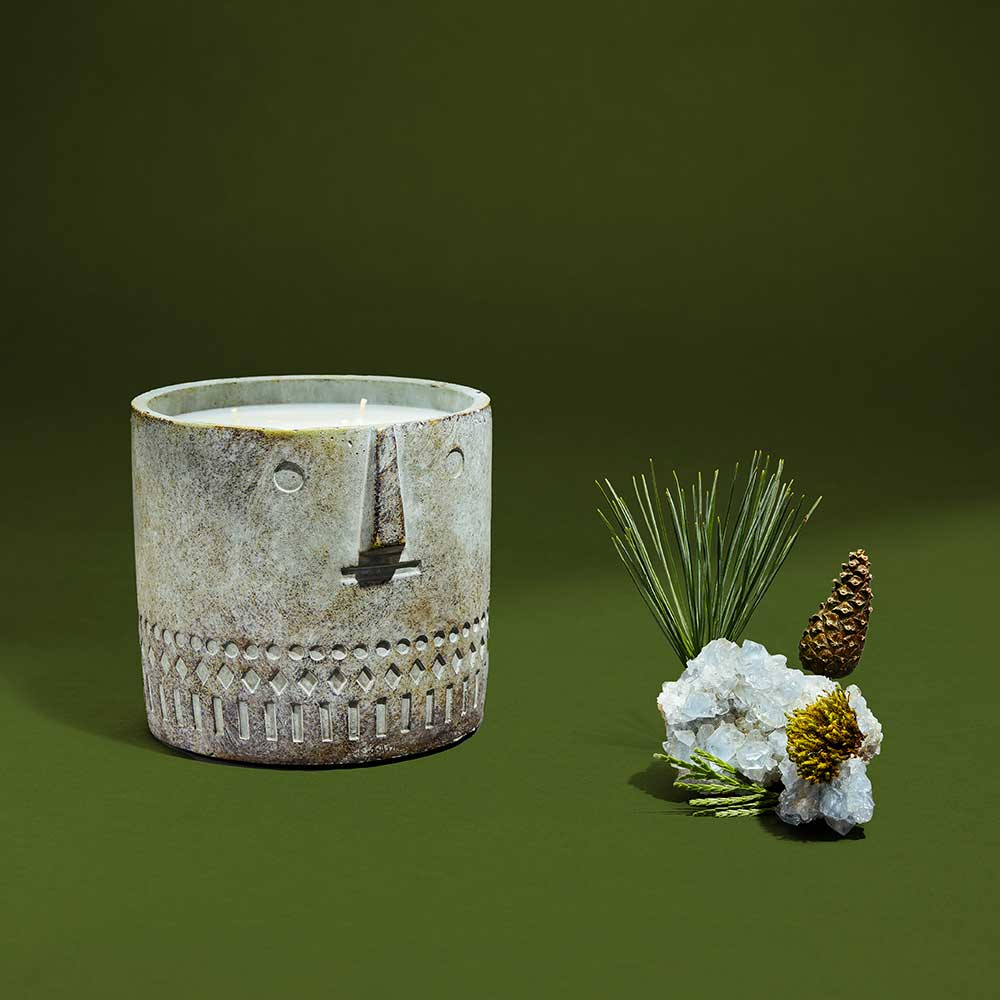Stone face candle with a bear design displayed outdoors beside pine needles, showing its handmade cement vessel.