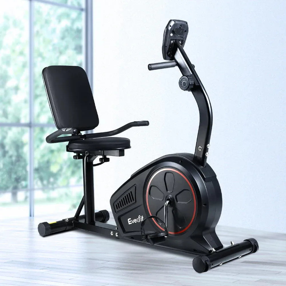 Full view of the black recumbent exercise bike placed on a wooden floor in a home gym setting.