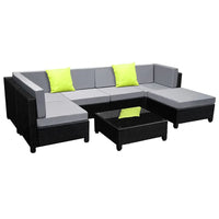Outdoor 7-piece wicker sofa set with dark cushions and square glass coffee table in backyard setting.