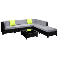 Square outdoor coffee table with tempered glass top beside dark wicker sofa with cushions.