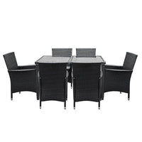 Glass-top outdoor dining table with aluminum frame, surrounded by cushioned rattan chairs