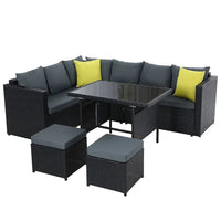 Black outdoor patio set including sofa with cushions, ottoman, and table on a stone patio.
