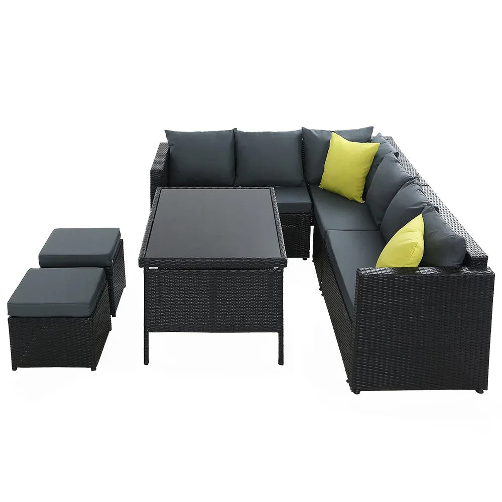 Black wicker patio dining set arranged with double seats and ottoman under bright outdoor light.