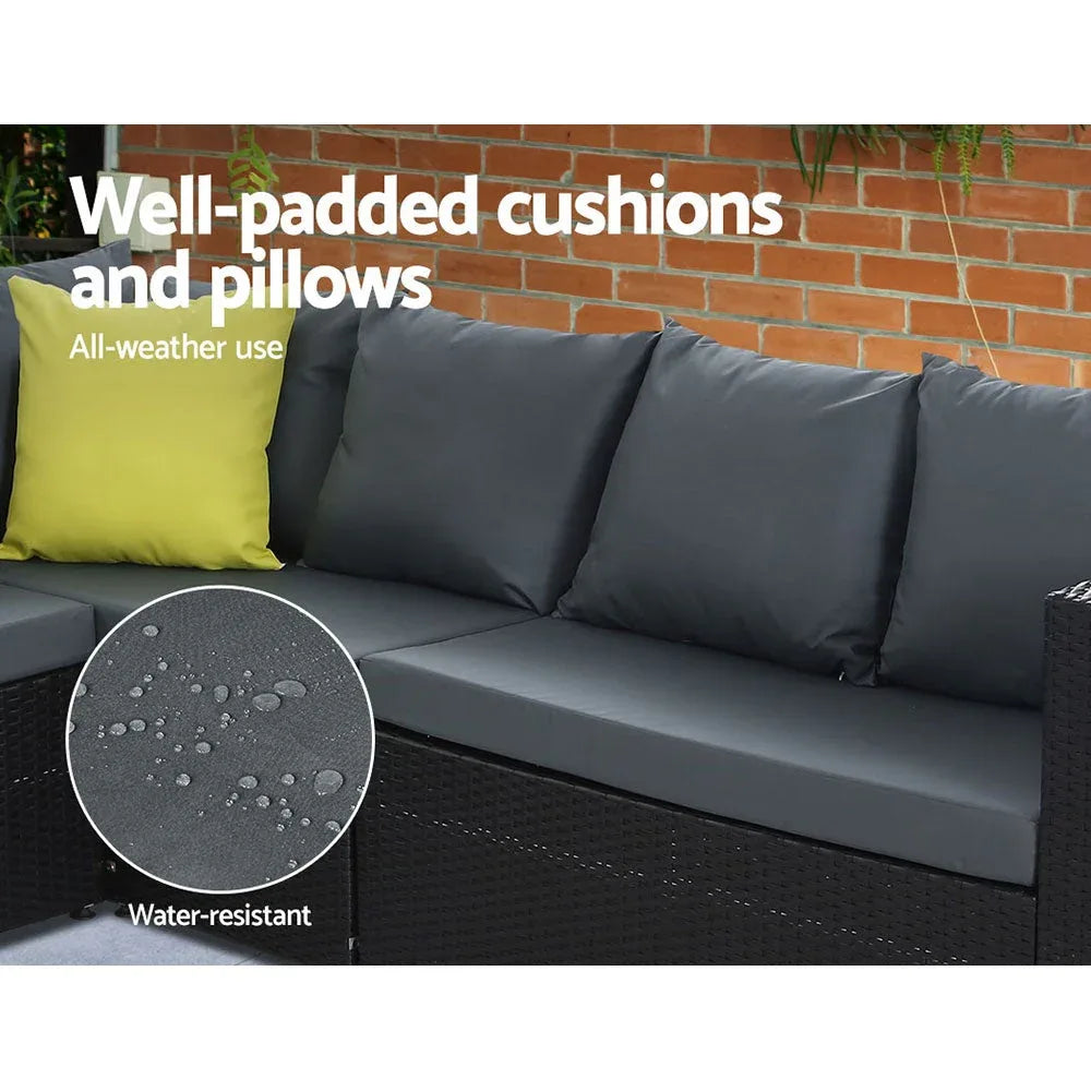 Modern black outdoor dining sofa set on stone floor with cream cushions and ottoman.