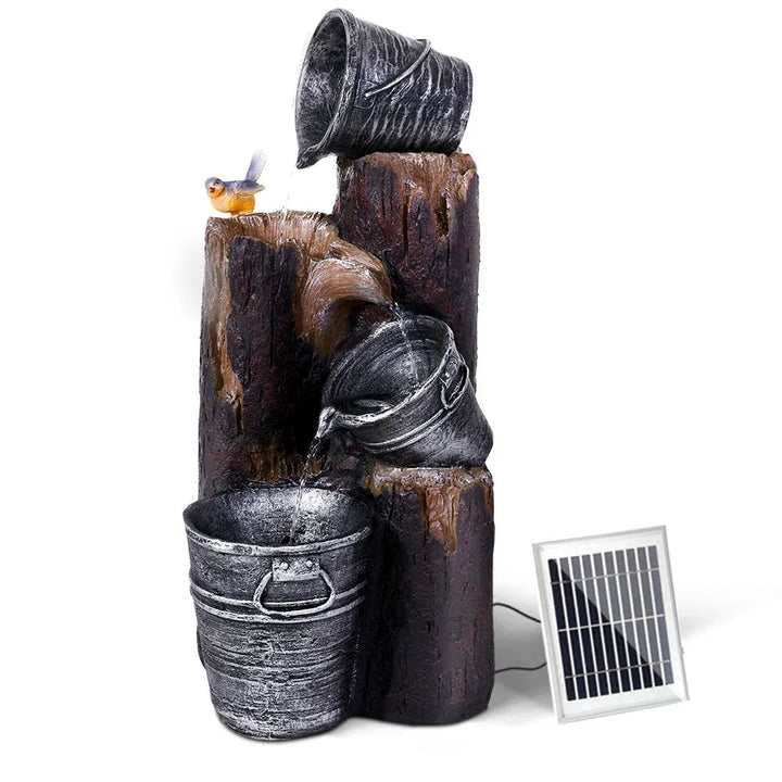 Three-tier black solar bird bath fountain with water flowing over each bucket-shaped tier in a garden setting.