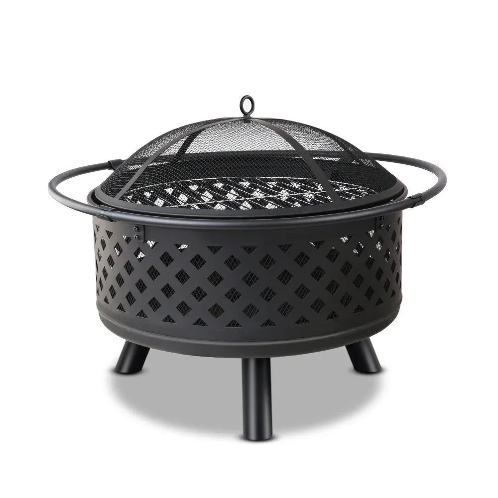 Diamond pattern metal fire pit with glowing fire inside on a patio at night.