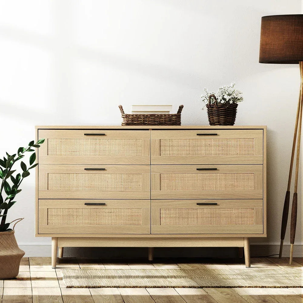 Styled bedroom setting with tallboy rattan chest alongside bed and lamp.