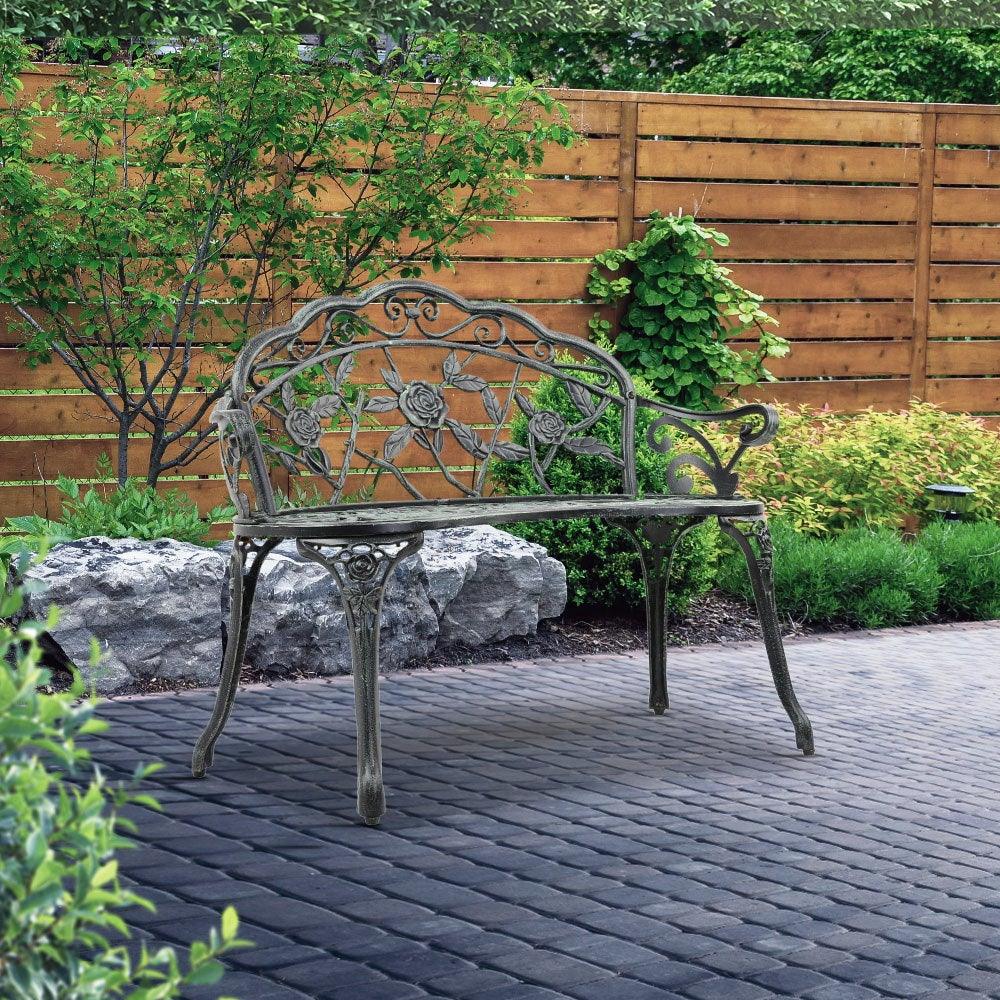 Full view of two-seat green Victorian garden bench with floral motif backrest outside.