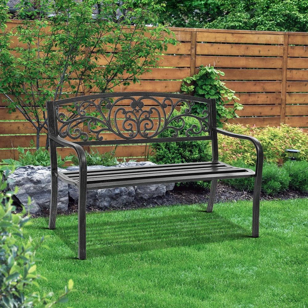 Black vintage-style garden bench on outdoor deck with greenery in background.