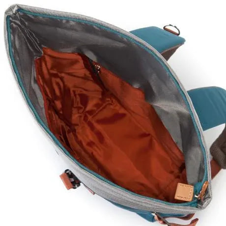 Blue rolltop backpack with rolled top and front zipper in simple studio setting.