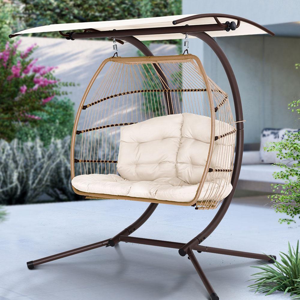 The complete Gardeon hanging pod chair with canopy in lush backyard setting at sunset.