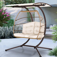 The complete Gardeon hanging pod chair with canopy in lush backyard setting at sunset.