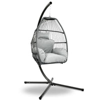 Grey hand-woven wicker hanging egg chair with rope suspension and padded cushion, shown outdoors.