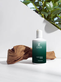 Bottle of Organic Hair Wash Aloe shampoo with aloe leaves and wheat grains on wooden surface.