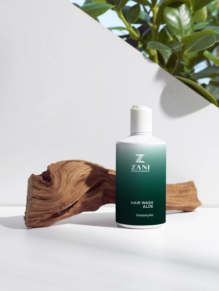 Bottle of Organic Hair Wash Aloe shampoo with aloe leaves and wheat grains on wooden surface.