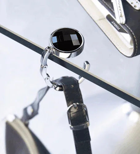 Close-up view of rhinestone handbag hanger with foldable arm on white background.