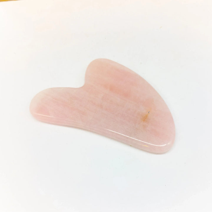 Rose quartz Gua Sha massage tool resting on a white surface with soft natural light