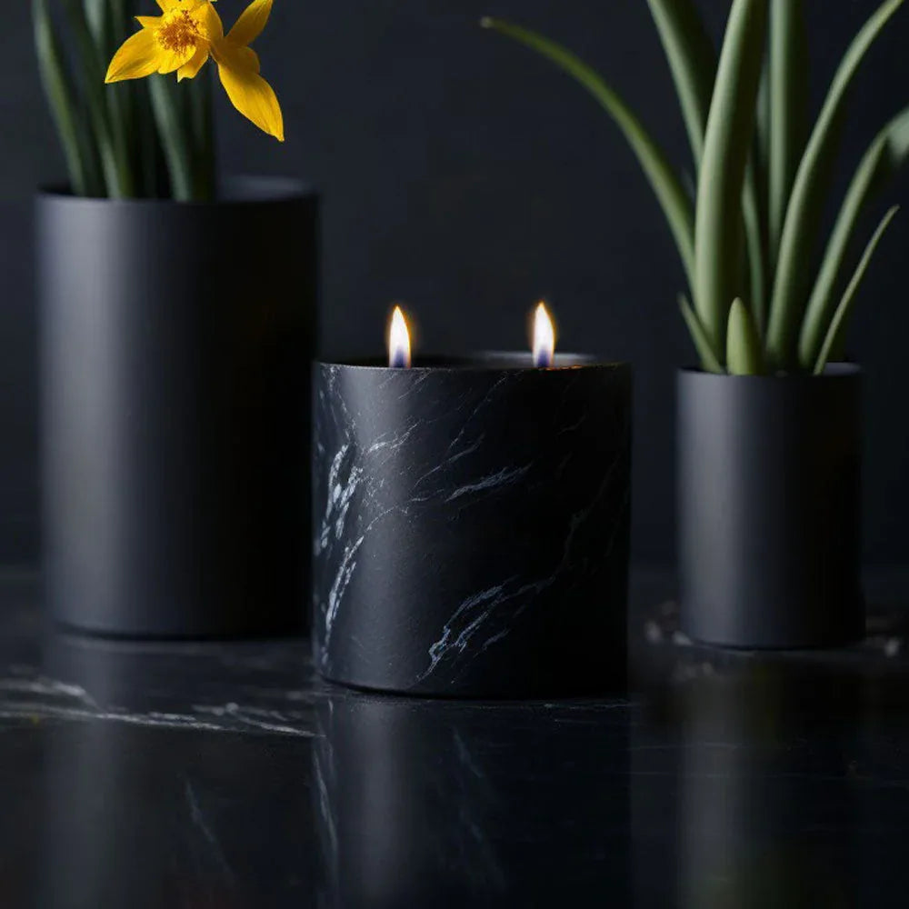 Black marquina candle burning on textured surface with soft natural light highlighting swirls.