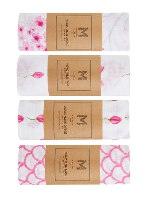 Set of four organic cotton muslin baby swaddles neatly folded with tissue paper and a ribbon.
